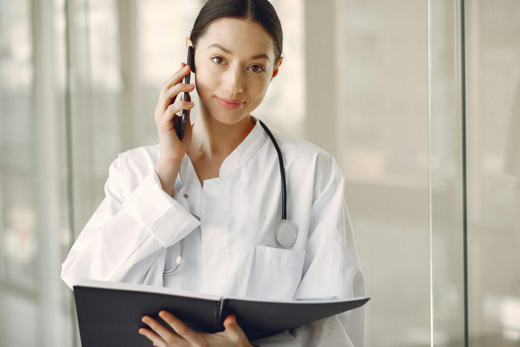Friendly female doctor speaking on the phone while holding a clipboard, symbolising support for health travel decisions.
